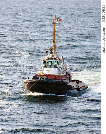 A tugboat navigates on the sea to assist a cruise ship entering the port 63260635