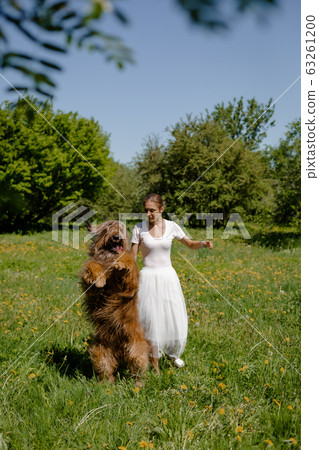 A young girl in a white dress is in the park with her pet dog briard. A young girl in a white dress is in the park with her pet dog briard. 63261200