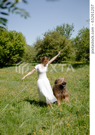 A young girl in a white dress is in the park with her pet dog briard. A young girl in a white dress is in the park with her pet dog briard. 63261207