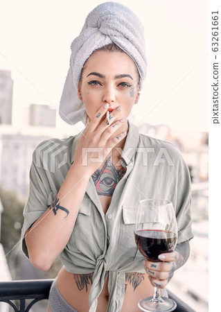 Young adult girl with cigarette and wine glass on balcony Young adult girl with cigarette and wine glass on balcony 63261661