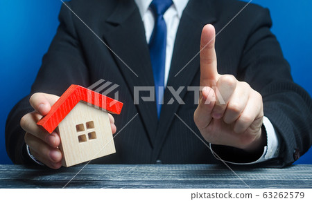 Man with a house makes a gesture of attention. Legal advice on terms a contract deal for purchase of real estate, lending and mortgage loan. Warning, indicate the nuances. Warn about risk of threat. Man with a house makes a gesture of attention. Legal advice on terms a contract deal for purchase of real estate, lending and mortgage loan. Warning, indicate the nuances. Warn about risk of threat. 63262579