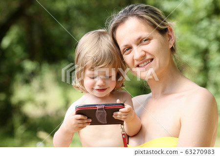 Happy little smiling child in the arms of the mother on a natural background Happy little smiling child in the arms of the mother on a natural background 63270983