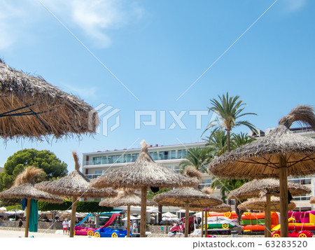 The beaches of Mallorca lined with beach umbrellas and beach beds made of straw under the clear and shining sun The beaches of Mallorca lined with beach umbrellas and beach beds made of straw under the clear and shining sun 63283520