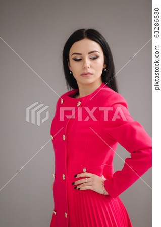Attractive brunette model in crimson dress on gray background in studio 63286880