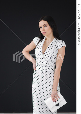 Beautiful model demonstrating white spring dress. Young brunette on black background 63286983