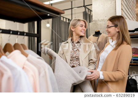 Two happy elegant females looking at one another while choosing new coat Two happy elegant females looking at one another while choosing new coat 63289019