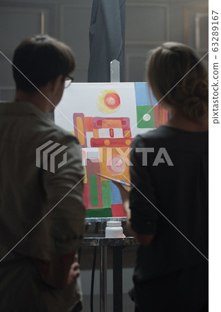 Young female student of art school and her teacher standing in front of easel Young female student of art school and her teacher standing in front of easel 63289167