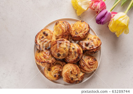 Homemade puff buns with custard cream and raisins in a ceramic plate on a light background. Nearby 63289744
