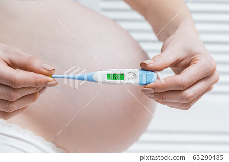 Pregnant woman holding electronic thermometer with 63290485
