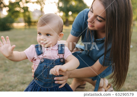 First step of adorable little girl in summer park. Mom and daughter walking First step of adorable little girl in summer park. Mom and daughter walking 63290579
