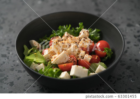 Healthy light salad with cherry tomatoes, mozzarella and frisee in black bowl on concrete surface 63301455