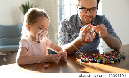 Smiling dad and small cute daughter making bracelets. 63303104