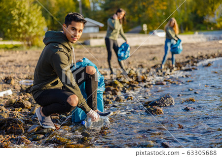 Man crouching while picking up garbage on shore Man crouching while picking up garbage on shore 63305688