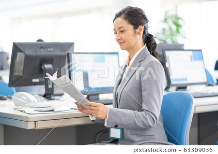 Middle-aged woman reading an English newspaper in the office 63309036