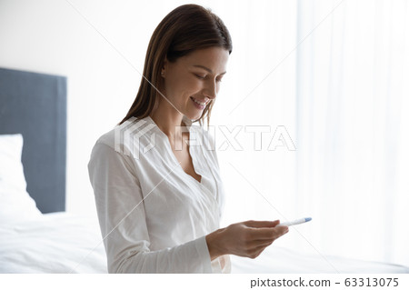 Smiling brunette lady in nightgown waiting for pregnancy confirmation. Smiling brunette lady in nightgown waiting for pregnancy confirmation. 63313075