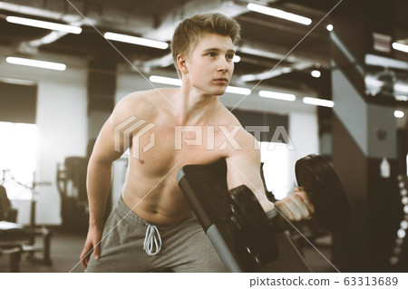 Closeup of a strength fitness man with dumbbell, having workout in the gym. Fit young man with beautiful torso. Beginner Bodybuilder and muscular body concept. 63313689