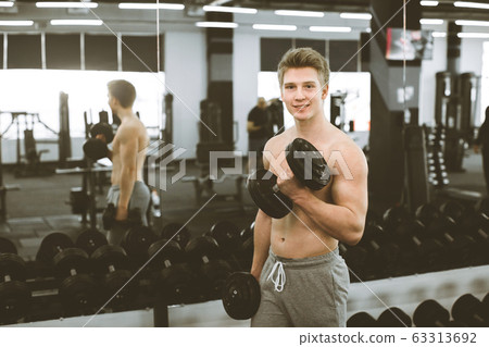 Portrait of young smiling muscular bodybuilder with dumbbells posing in modern fitness gym 63313692
