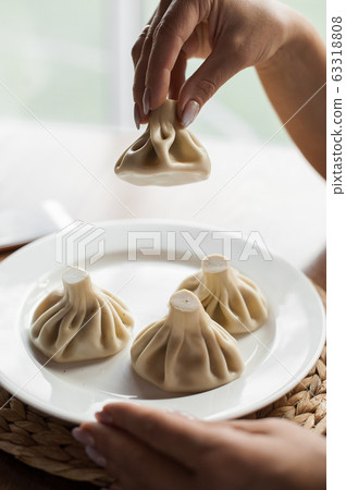 Georgian traditional Khinkali on white plate. One Khinkali held in woman hand. Georgian traditional Khinkali on white plate. One Khinkali held in woman hand. 63318808