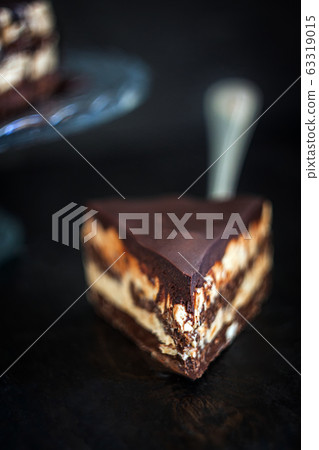 Slice and chocolate cake layers with butter-cream-nut cream with chocolate drips on a glass stand on 63319015