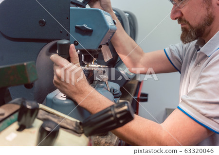 Locksmith cutting key with his machine 63320046