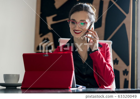 Businesswoman working with her computer while being on the phone Businesswoman working with her computer while being on the phone 63320049