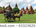 Horse drawn carriage tourists is driving along in front of the ancient temple of Bagan, Myanmar.  63323620