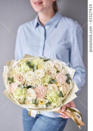 European floral shop. Beautiful bouquet of mixed flowers in woman hands. Work of the florist at a flower shop. Delivery fresh cut flower. 63327419
