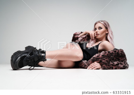 Blonde woman in leopard coat and boots looking at side while lying in studio 63331915