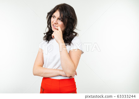 brunette girl in a white t-shirt worries and bites her nails from stress on a white background brunette girl in a white t-shirt worries and bites her nails from stress on a white background 63333244