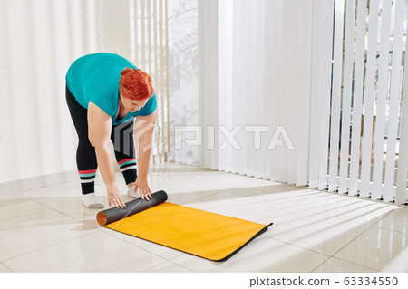 Woman rolling up yoga mat Woman rolling up yoga mat 63334550