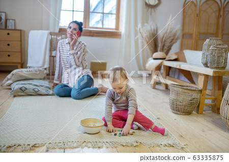 Daughter playing with artificial stones, mom talking on the phone Daughter playing with artificial stones, mom talking on the phone 63335875