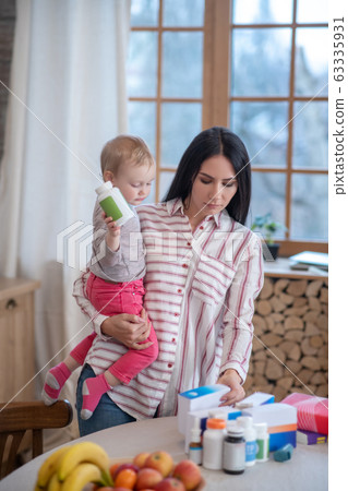 Mom standing, holding her daughter, choosing medicine 63335931