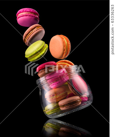 Flying french colorful macaroons and jar on wooden table isolated on black Flying french colorful macaroons and jar on wooden table isolated on black 63336263