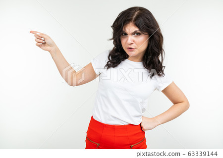 close-up of brunette girl in white t-shirt shows on space with index finger on a white studio close-up of brunette girl in white t-shirt shows on space with index finger on a white studio 63339144