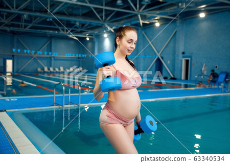 Pregnant woman holds dumbbells at the poolside Pregnant woman holds dumbbells at the poolside 63340534