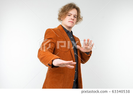 confident curly blond guy in a brown jacket with arms crossed refuses on a white studio background 63340538