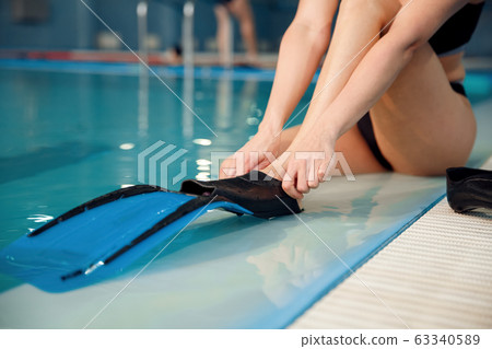 Female swimmer puts on flippers at the poolside Female swimmer puts on flippers at the poolside 63340589