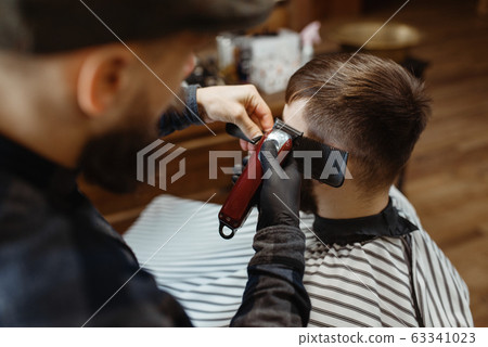Barber in hat cuts the client 's hair, barbershop 63341023