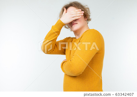 serious wavy blond young man standing thoughtfully with his eyes closed on a white background 63342407
