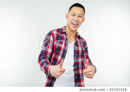 smiling asian guy in a checkered shirt wide open showing like thumb up on an isolated white studio 63342426