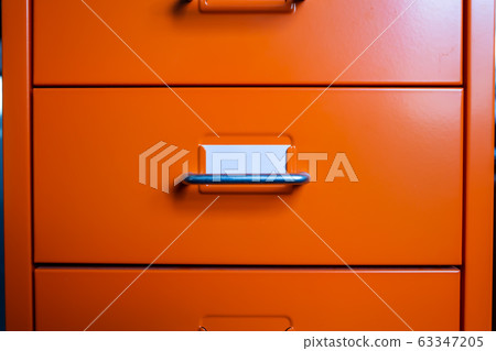 Filing cabinet with closed drawer, A white card for write letter, Orange metal colour, Administration and storage concept, closeup & Macro shot 63347205