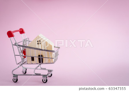 Wooden house model in the shopping cart on pink background Wooden house model in the shopping cart on pink background 63347355