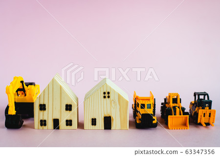 A yellow toy heavy machinery with wooden house model on pink background A yellow toy heavy machinery with wooden house model on pink background 63347356