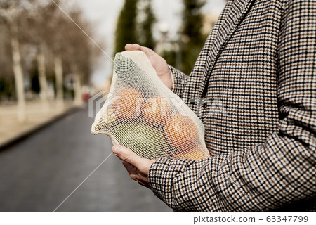 man carrying a mesh bag full of fruit and vegs man carrying a mesh bag full of fruit and vegs 63347799