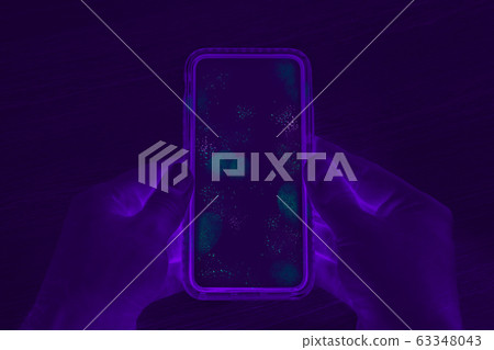 Hands holding cell phone with dirty contaminated touch screen - UV Blacklight exposing infectious 63348043
