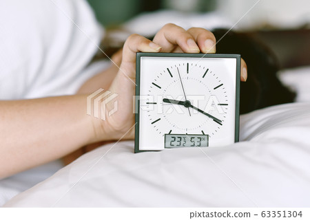 Sleepy girl's hand showing alarm clock and waking up late in the morning Sleepy girl's hand showing alarm clock and waking up late in the morning 63351304