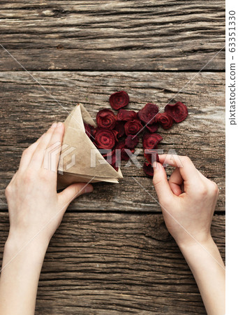 Home-made beet chips. Snacks are wrapped in a paper bag. Hand holds food bag. Handmade healthy vegetables chips 63351330