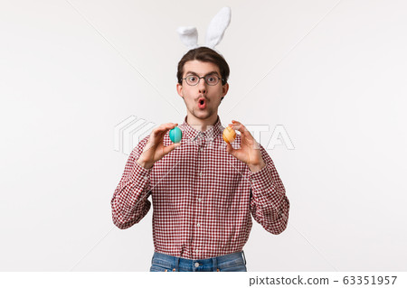 Traditions, religious holidays, celebration concept. Amused enthusiastic handsome young man suggest girlfriend play Easter game on family gathering party, hold two painted eggs, wear rabbit ears Traditions, religious holidays, celebration concept. Amused enthusiastic handsome young man suggest girlfriend play Easter game on family gathering party, hold two painted eggs, wear rabbit ears 63351957