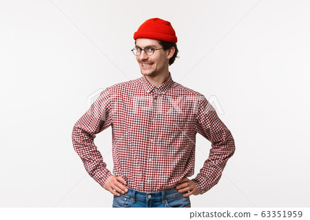 Waist-up portrait upbeat and enthusiastic young hipster guy in red beanie and glasses, with checked shirt, standing ready with confident straight pose, hold hands on waist and smiling camera Waist-up portrait upbeat and enthusiastic young hipster guy in red beanie and glasses, with checked shirt, standing ready with confident straight pose, hold hands on waist and smiling camera 63351959
