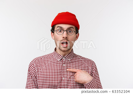 Close-up portrait surprised young hipster guy in glasses and beanie staring with disbelief, pointing himself indecisive, dont know if person for real mentioned him, standing white background Close-up portrait surprised young hipster guy in glasses and beanie staring with disbelief, pointing himself indecisive, dont know if person for real mentioned him, standing white background 63352104